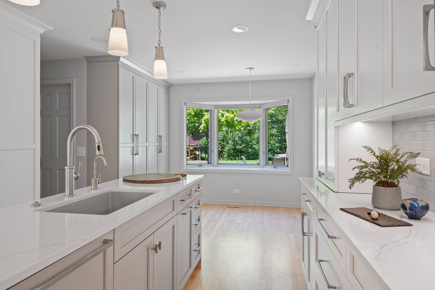 A kitchen with white cabinets , a sink , and a window.