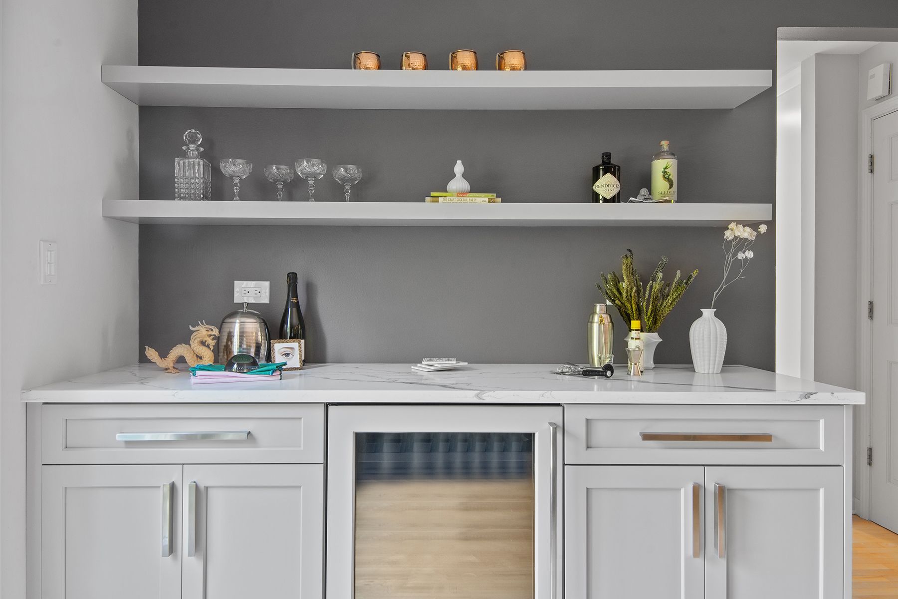 A kitchen with white cabinets , a refrigerator , shelves and a bar.