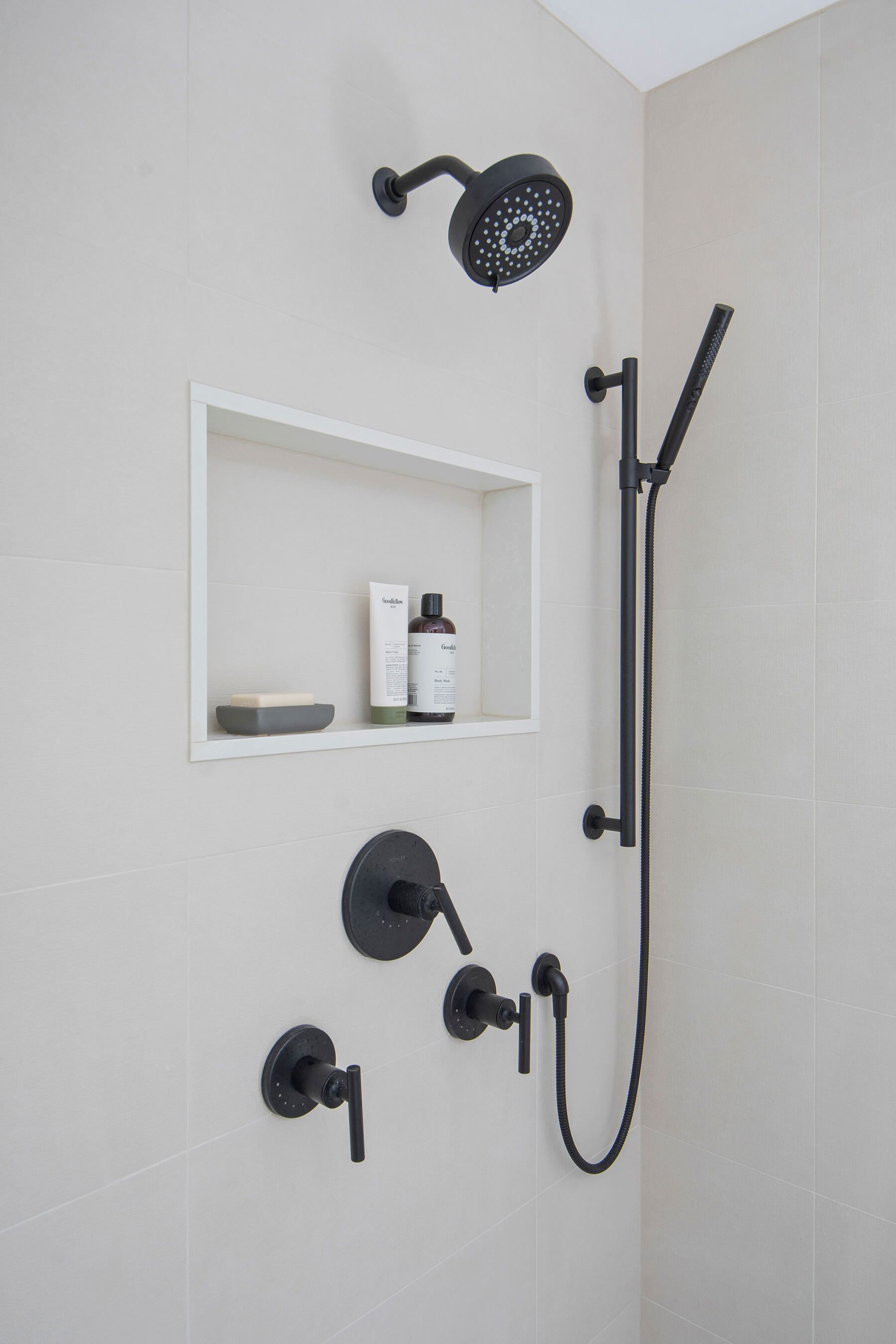 A shower with a black shower head and a soap dish.