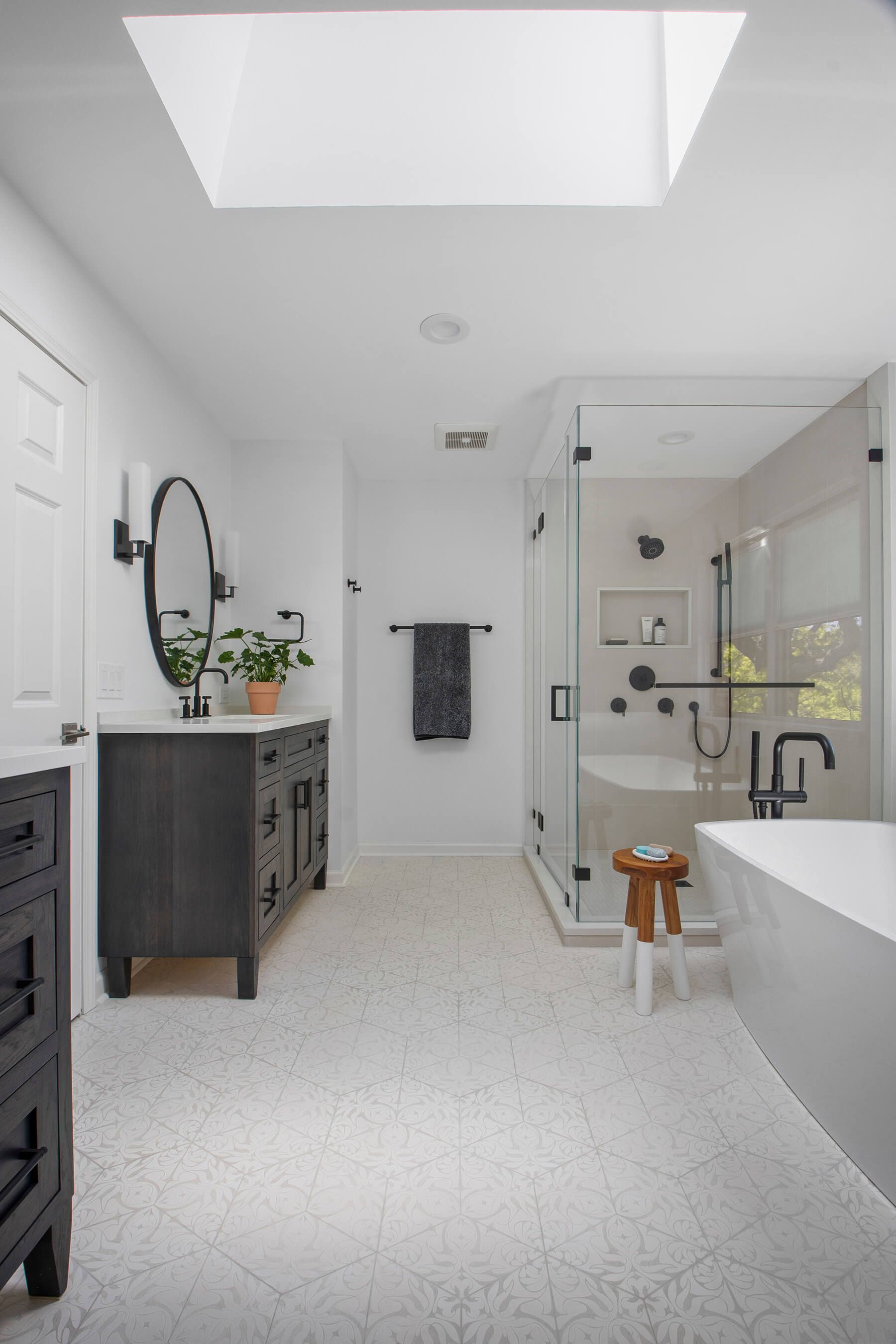A bathroom with a tub , sink , mirror and skylight.