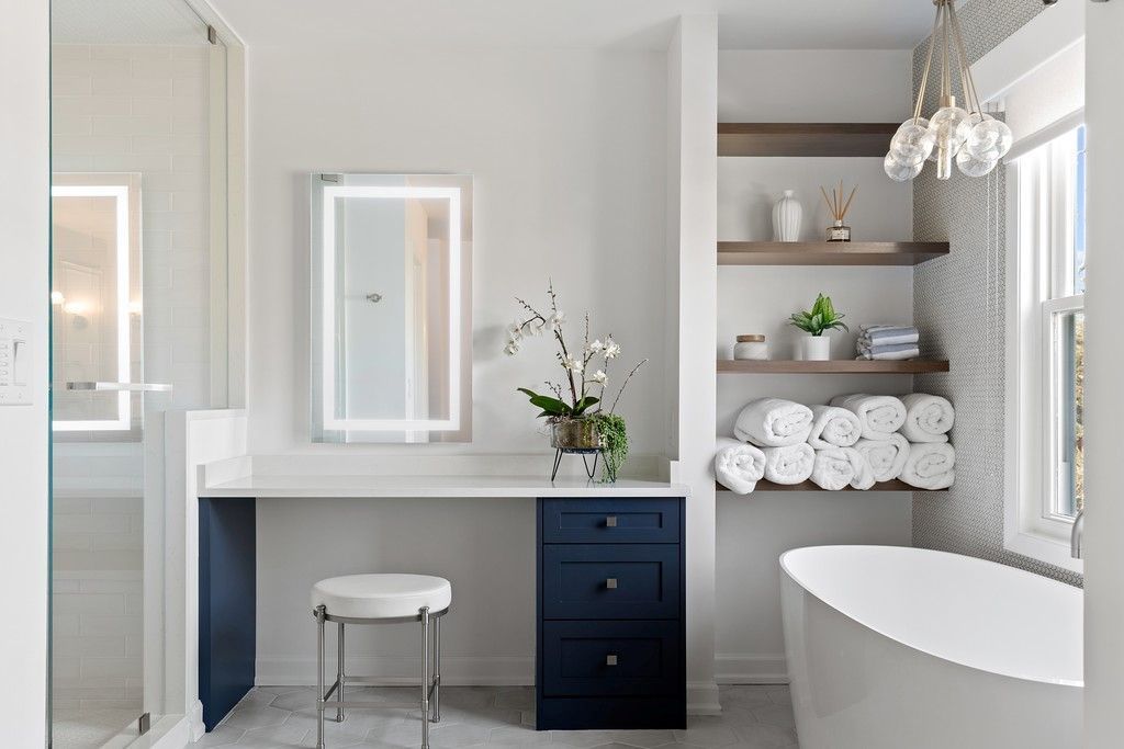 A bathroom with a tub , vanity , mirror and shelves.