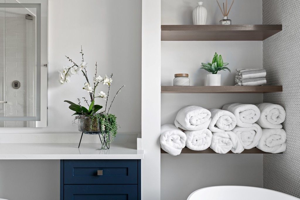 A bathroom with a tub , sink , mirror and shelves filled with towels.