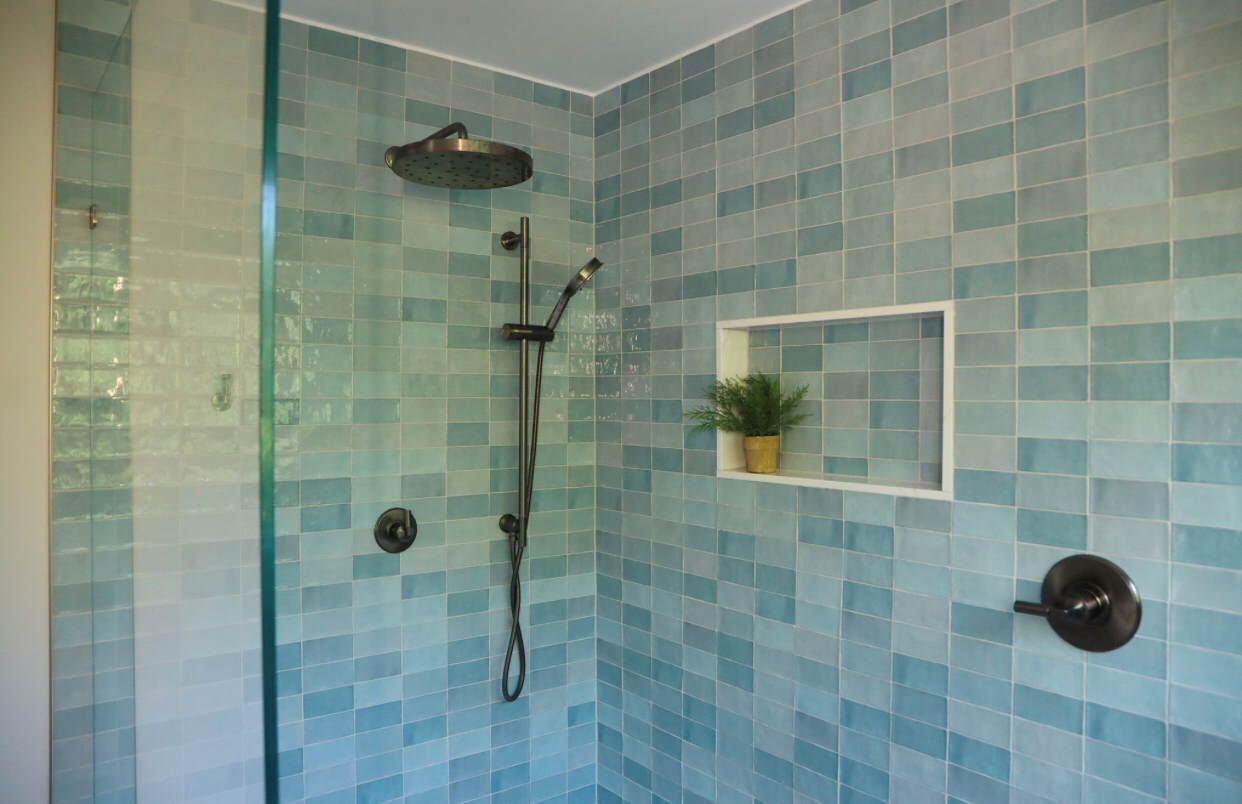 A shower with blue tiles and a plant in a niche.