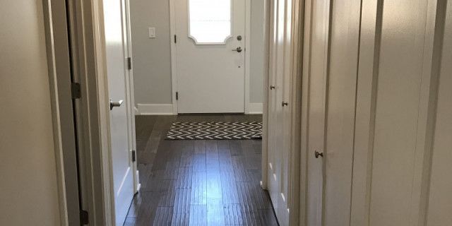 A hallway in a house with hardwood floors and white doors leading to the front door.