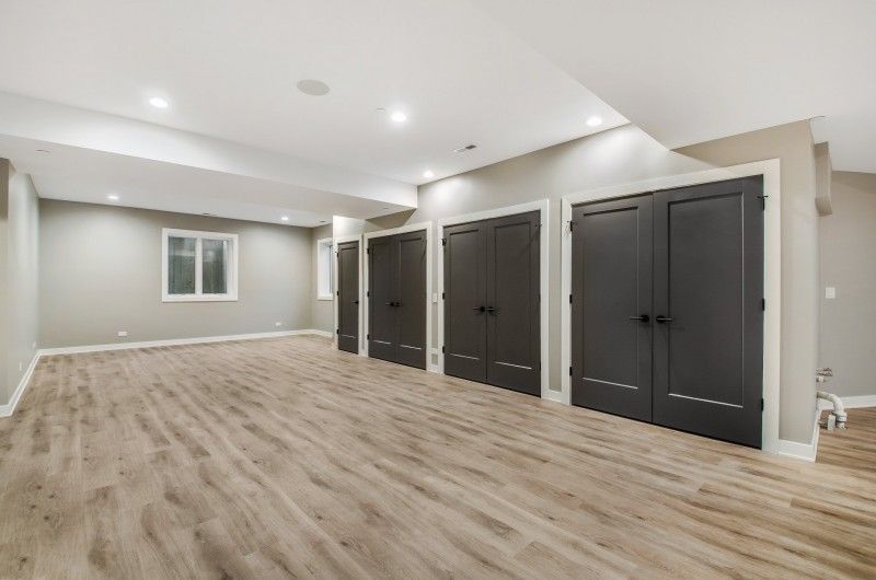 An empty basement with hardwood floors and black doors.