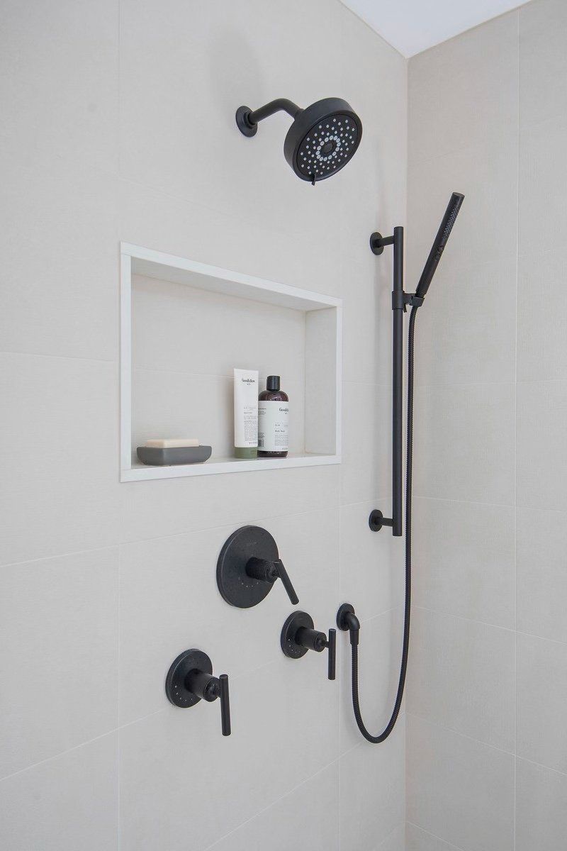 A shower with a black shower head and a white shelf.