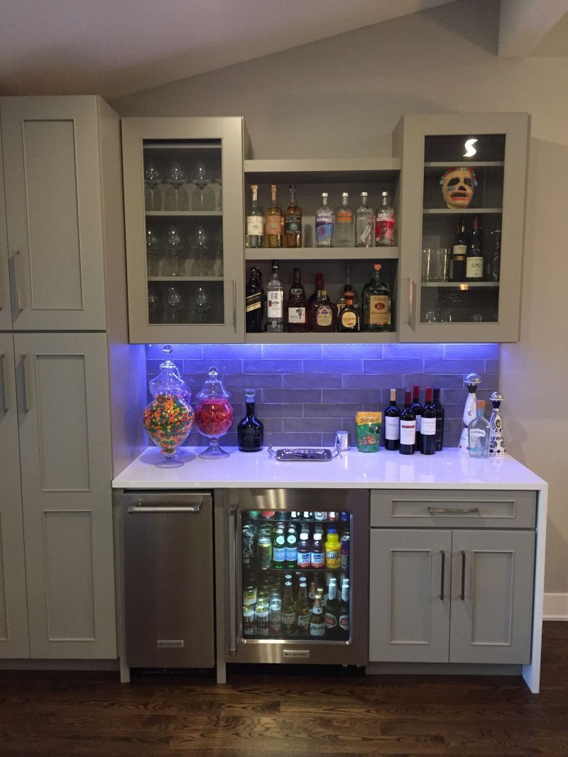 A kitchen with a bar and a refrigerator filled with bottles of alcohol.