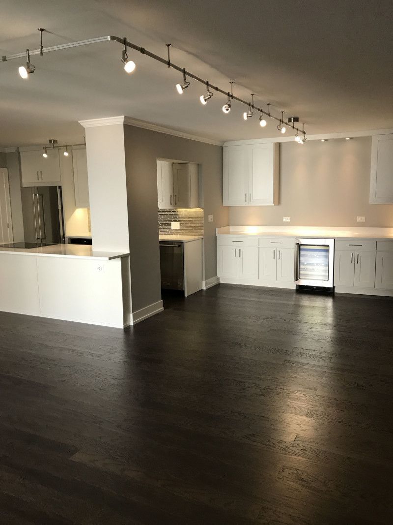An empty kitchen with white cabinets and dark wood floors