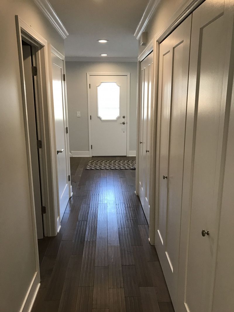 A long hallway with hardwood floors and white doors leading to a door.