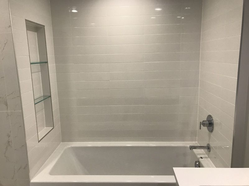 There is a bathtub in the bathroom with white tiles.