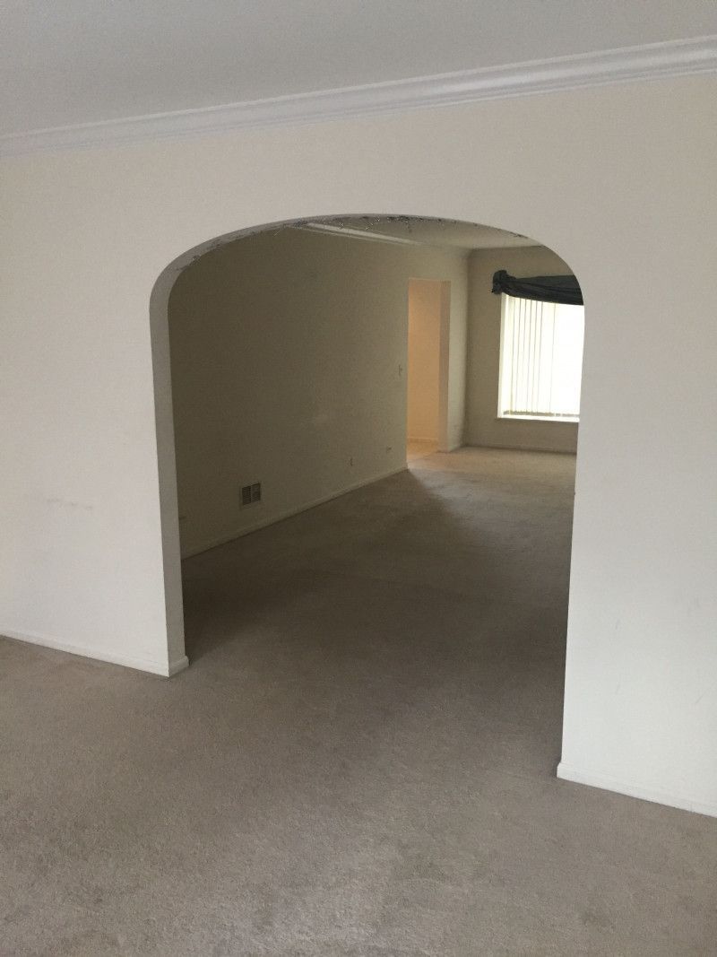 An empty living room with a carpeted floor and white walls.