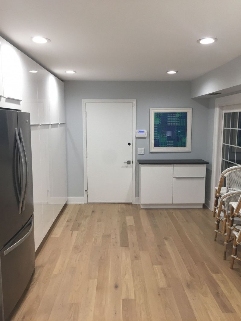 A kitchen with hardwood floors , white cabinets , a refrigerator and a picture on the wall.