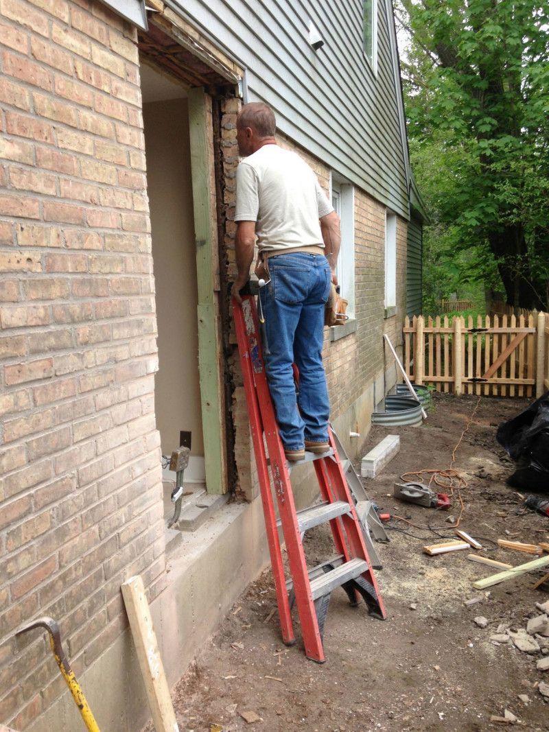 A man is standing on a ladder next to a brick wall.