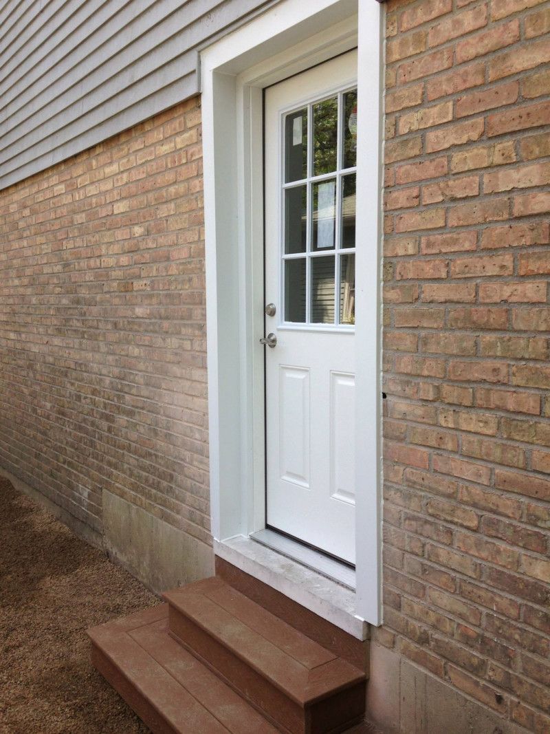 A white door is on a brick wall with wooden steps.