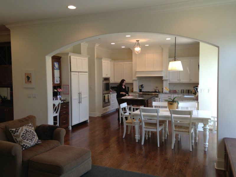 A living room with a table and chairs and a woman in the kitchen