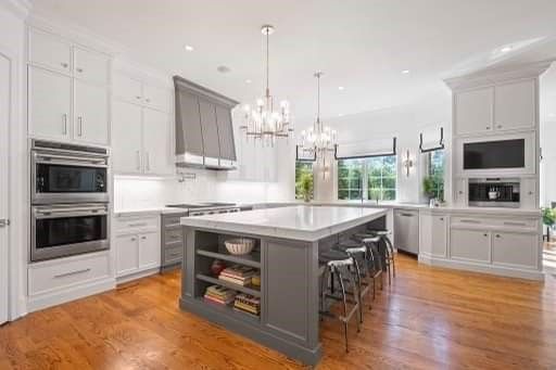 A kitchen with white cabinets , stainless steel appliances , hardwood floors and a large island.