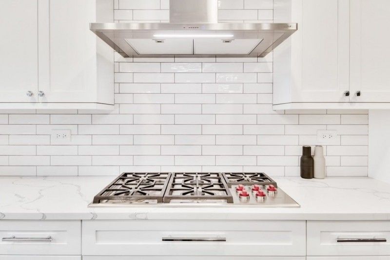 A kitchen with white cabinets and a stove top oven with a hood above it.