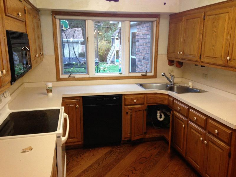 A kitchen with wooden cabinets , a stove , a sink , and a window.