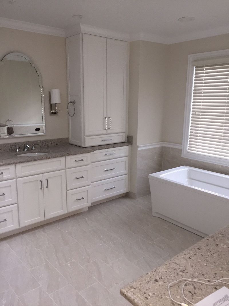 A bathroom with a tub , sink , mirror and cabinets.