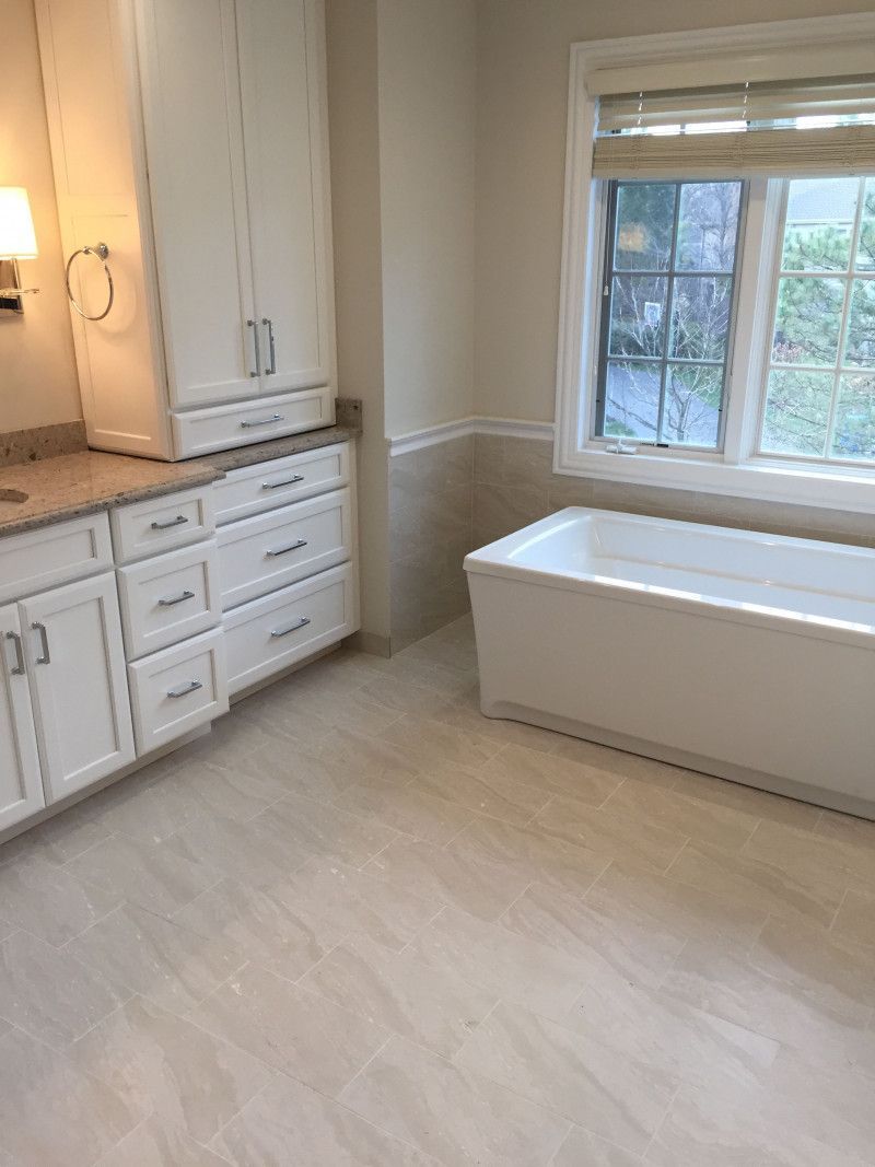 A bathroom with a tub , cabinets , and a window.
