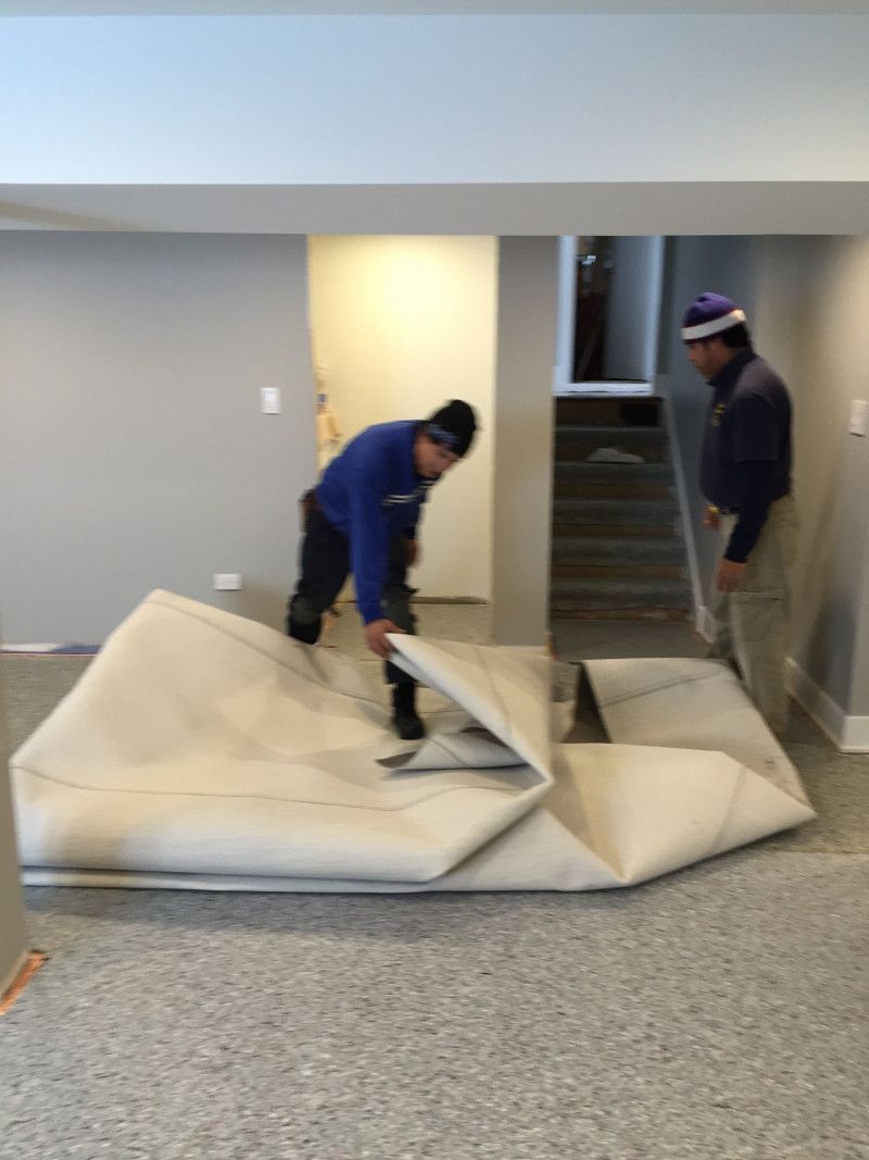 Two men are working on a carpet in a basement.