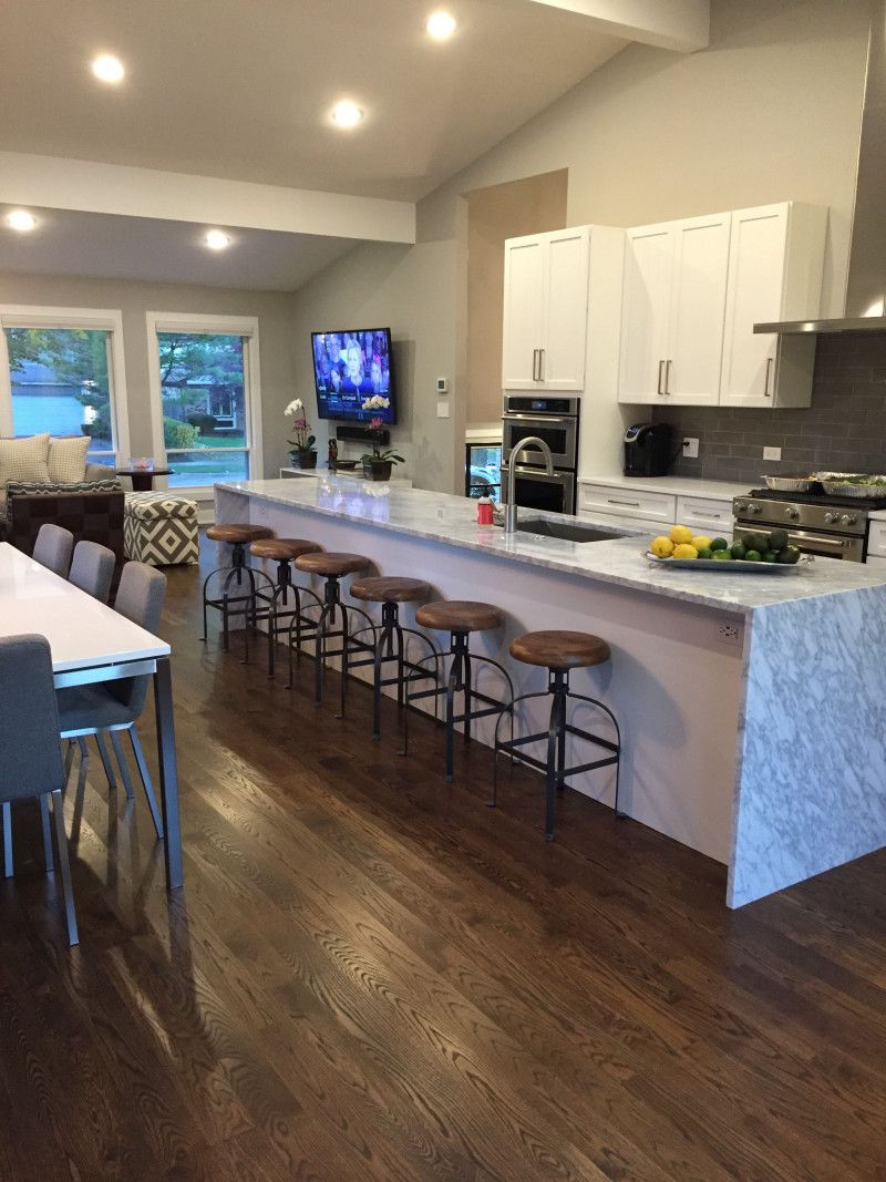 A kitchen with a long island , stools , a table and a television.