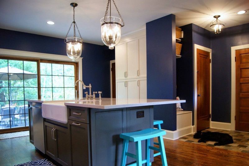 A kitchen with blue walls , white cabinets , a sink , and a blue stool.
