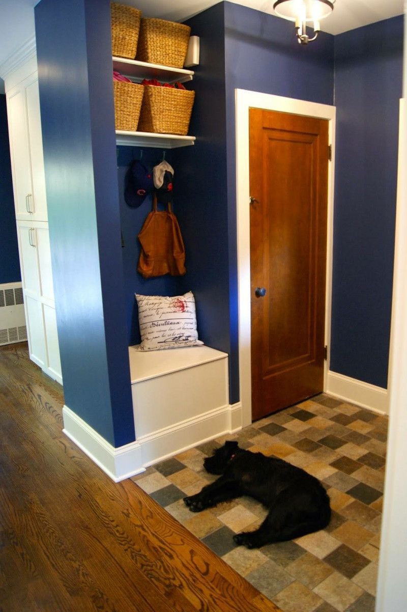 A black dog is laying on the floor in a hallway.