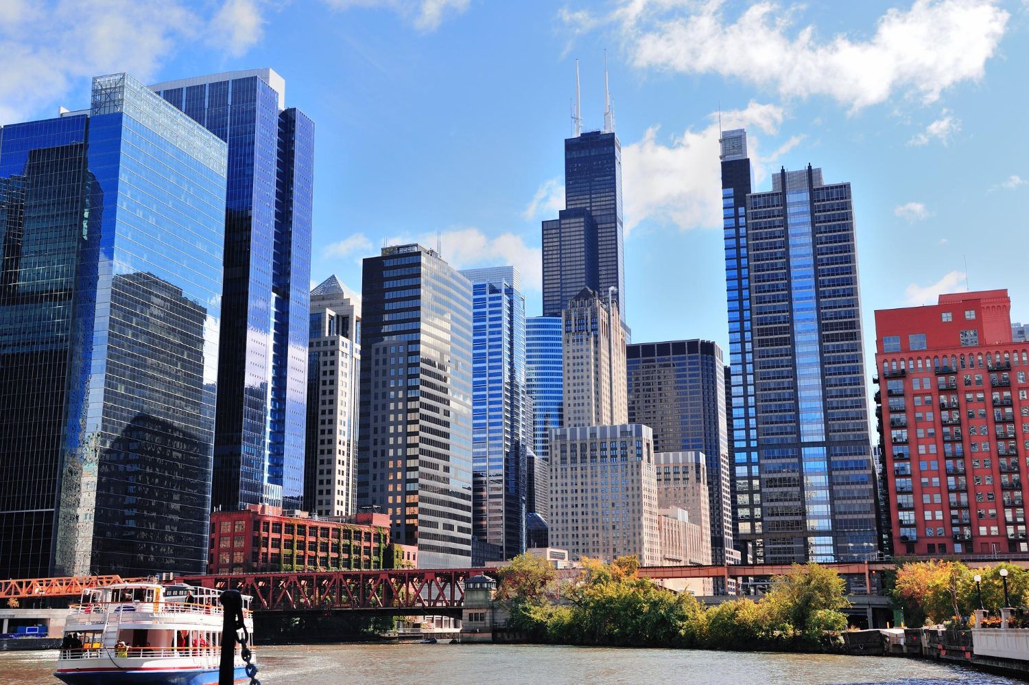 Chicago skyline with skyscrapers, a river, and a boat under a blue sky.