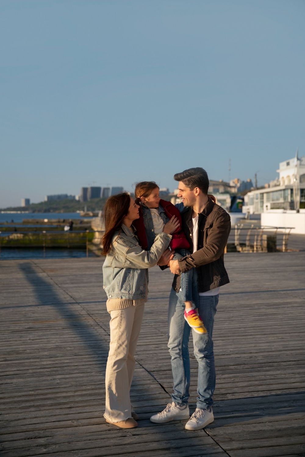 A family of three interacts outdoors. The man holds the child. The woman touches the child.