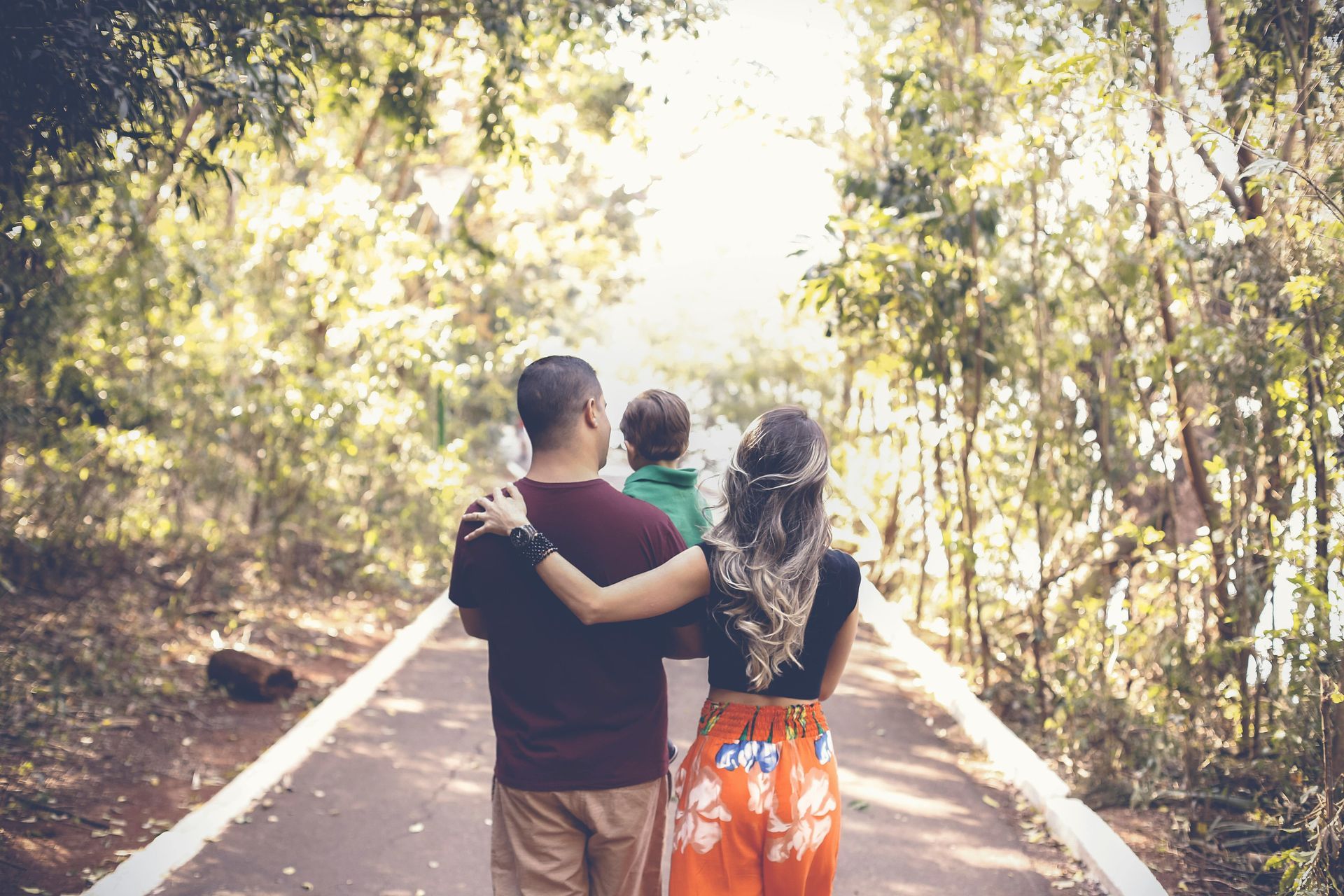 Family walking down a path in a park, arms around each other, sunny day.