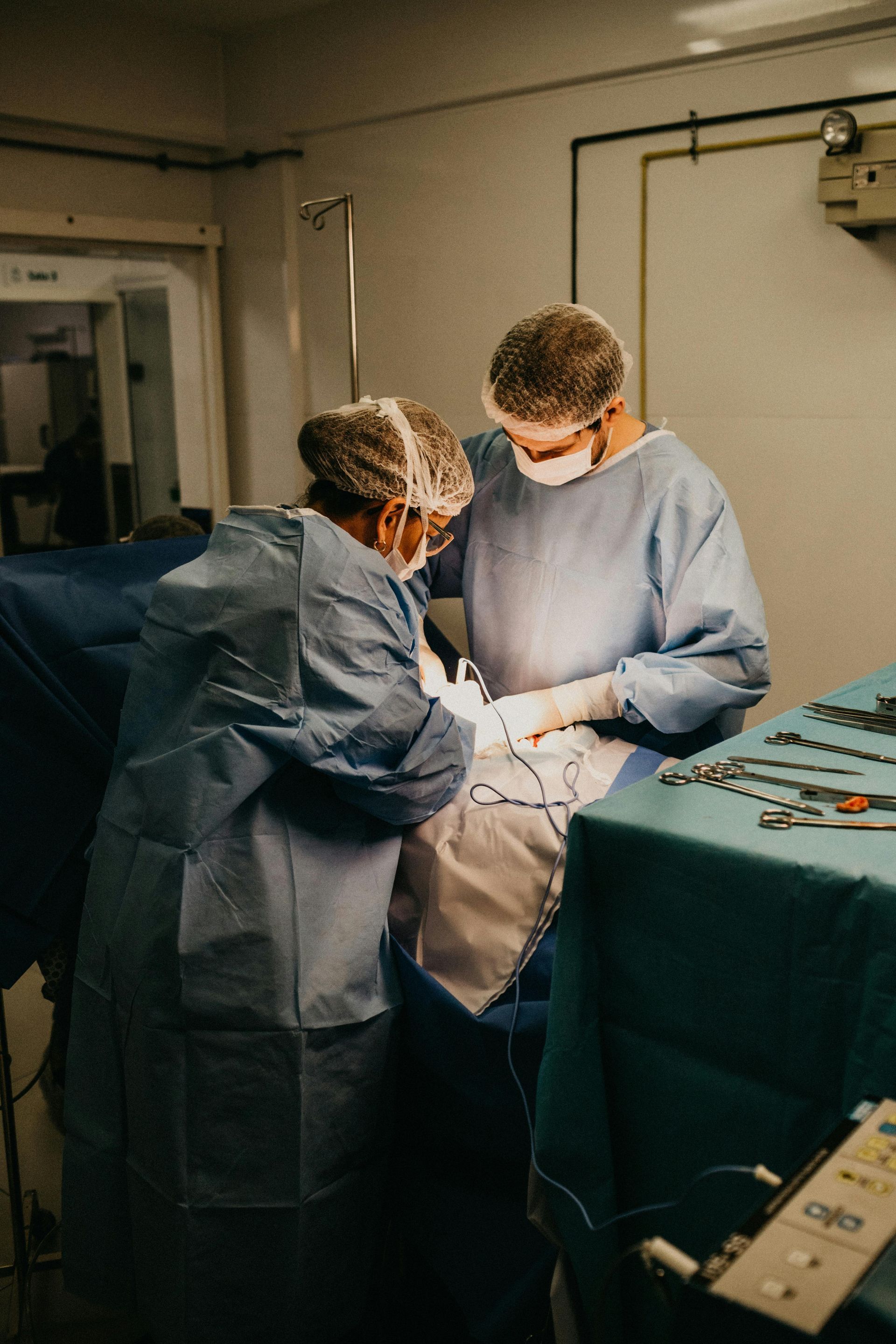 Two surgeons in blue scrubs operate under bright light in an operating room.