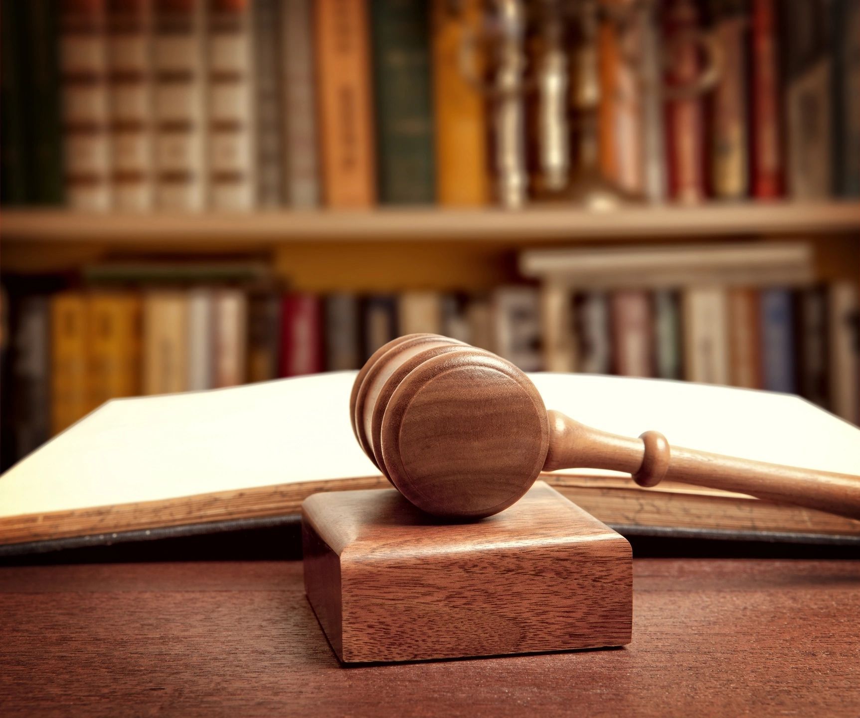 Wooden gavel on a block, open book in the background; bookshelf filled with books.