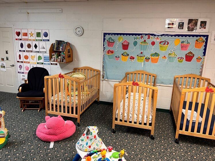 A room with a lot of cribs and a bulletin board with cupcakes on it.