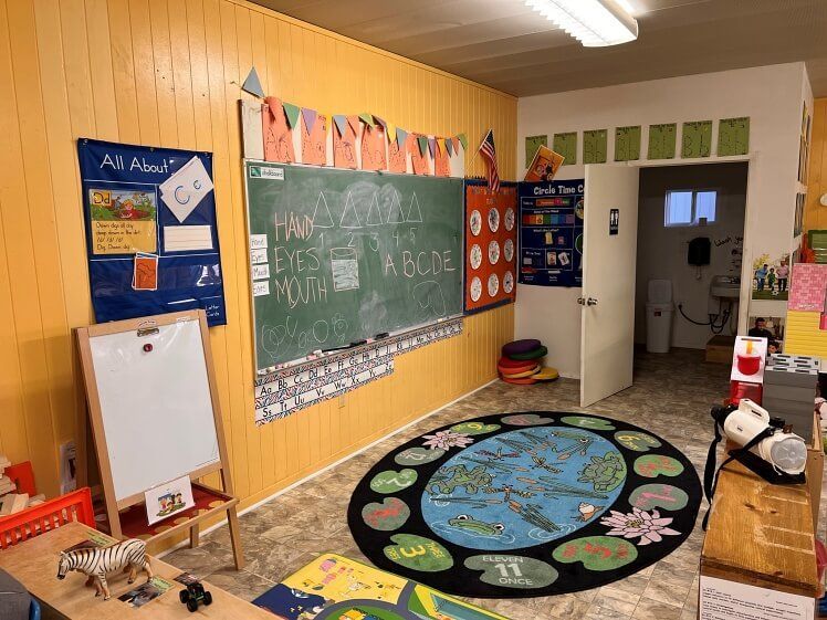 A classroom with a chalkboard and a rug.