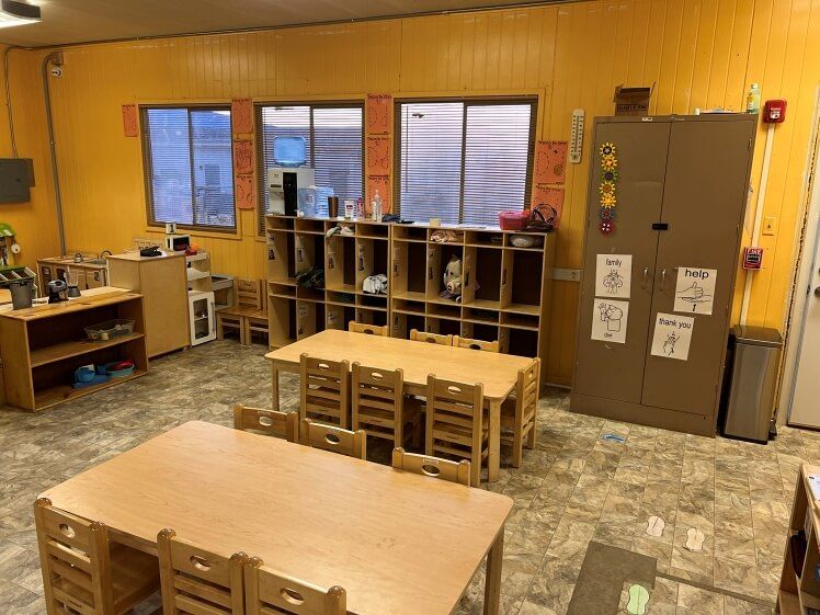 A classroom with wooden tables and chairs and yellow walls.