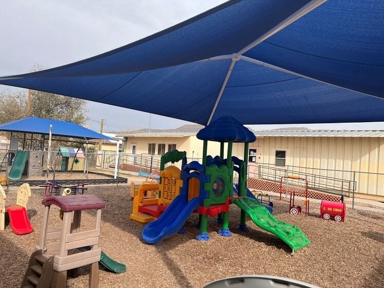 A playground with a blue umbrella over it and a slide.