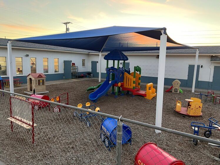 A playground with a blue umbrella and a mailbox in the foreground.