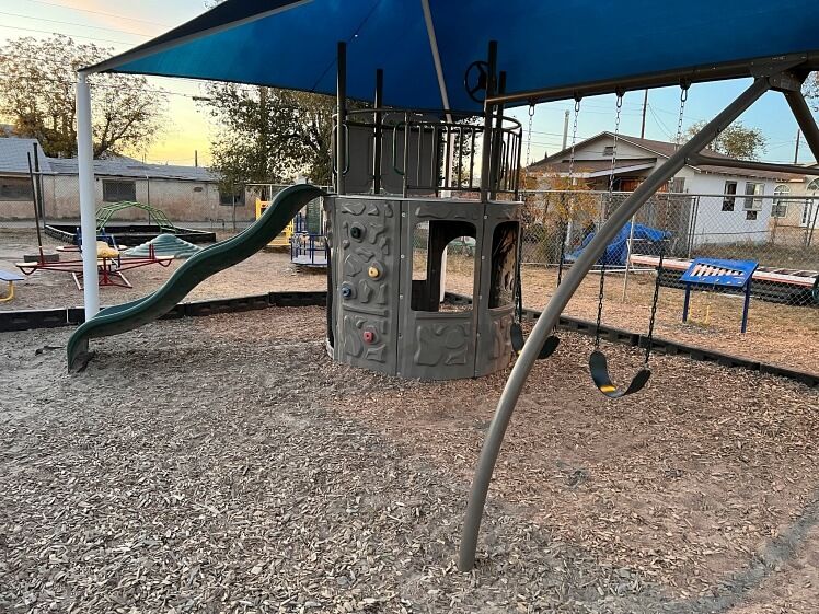 A playground with a slide and swings under a blue umbrella.