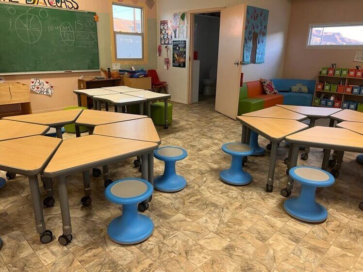 A classroom with wooden tables and blue stools.