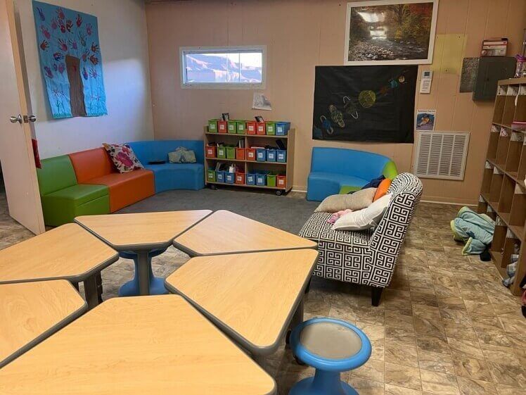 A classroom with tables , chairs , and a blackboard.