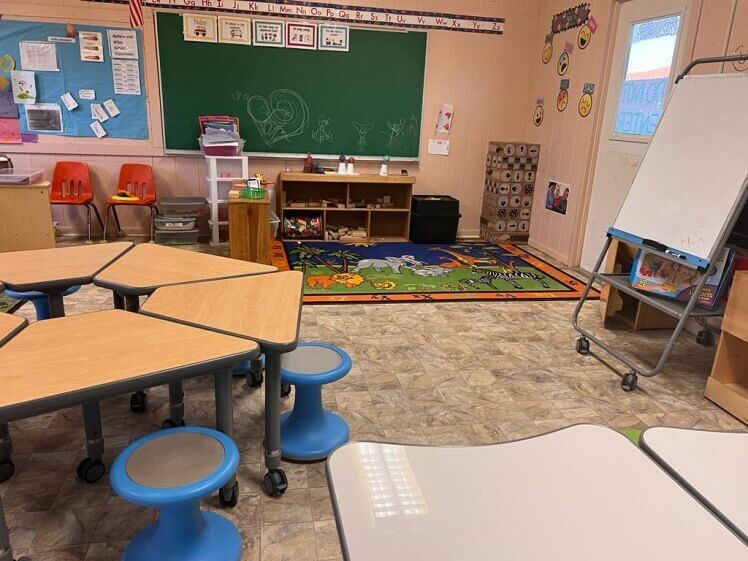 A classroom with tables and stools and a chalkboard.