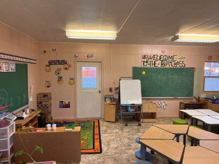 A classroom with tables , chairs , a blackboard and a door.