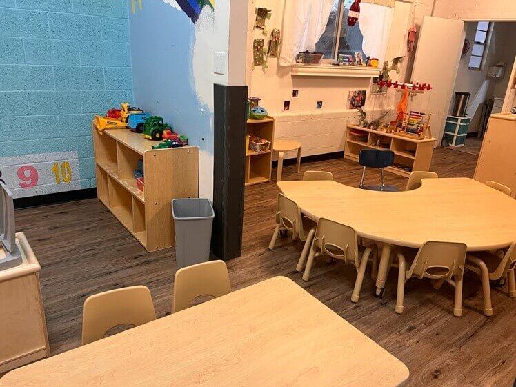 A classroom with tables and chairs and toys on the shelves.
