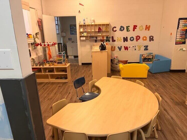A classroom with a table and chairs and the alphabet on the wall.