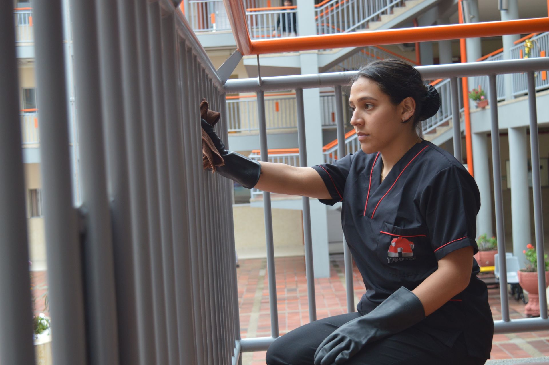 Una mujer con una blusa negra y guantes negros está limpiando una barandilla.