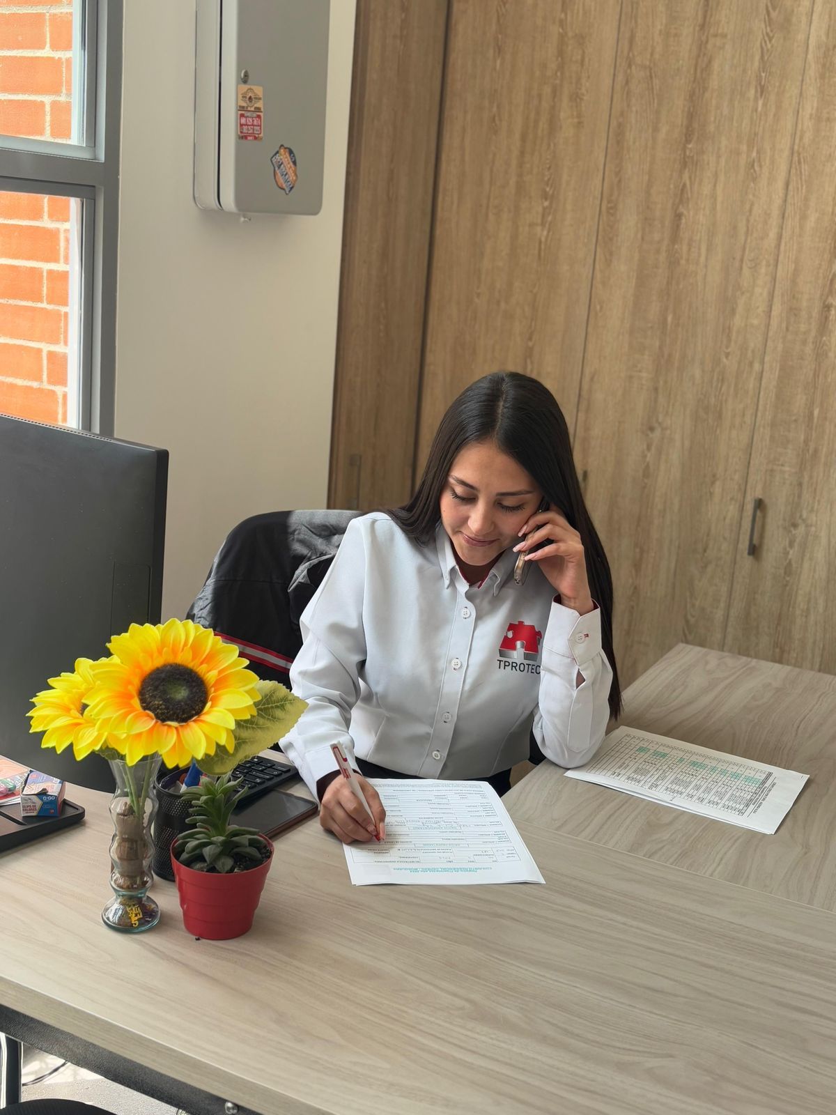 Una mujer está sentada en un escritorio hablando por un teléfono celular.