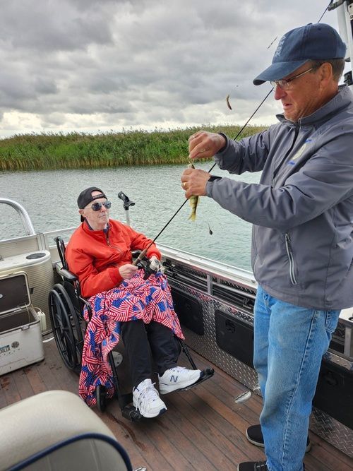 A man is fishing with a woman in a wheelchair on a boat.