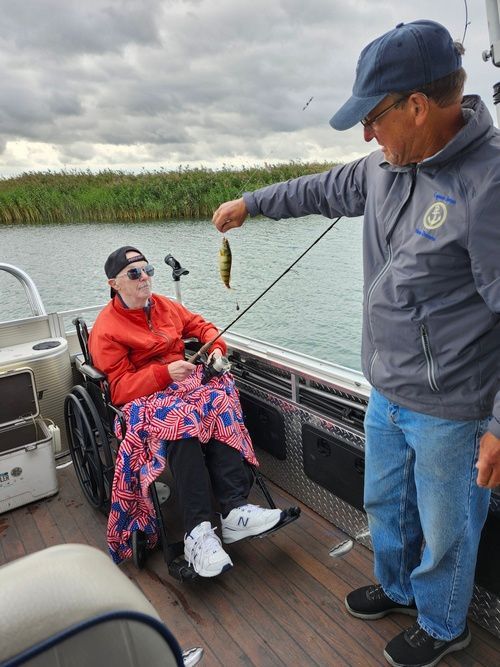 A man is fishing with a woman in a wheelchair on a boat.