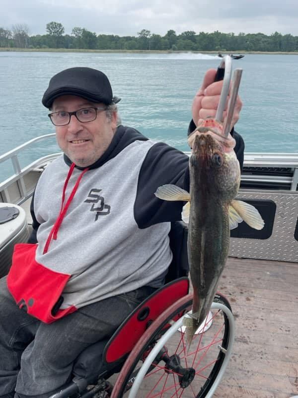 A man in a wheelchair is holding a fish on a boat